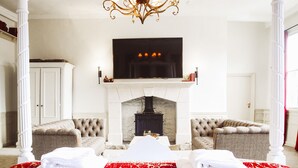 A bedroom with a fireplace, two armchairs, a bed with a red and white patterned bedspread, and a television above the fireplace. - The Old Crown Coaching Inn (Faringdon)
