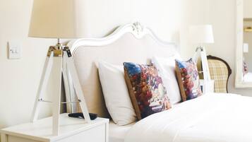 Una cama bien hecha con ropa de cama blanca y almohadas decorativas, una mesita de noche con lámpara y un enchufe de pared.