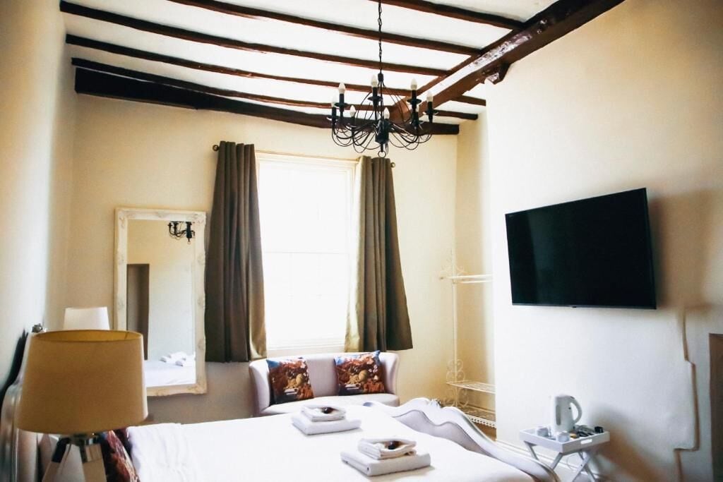 Quarto de hotel com cama, televisão, mesa de cabeceira, abajur e janela com cortinas.