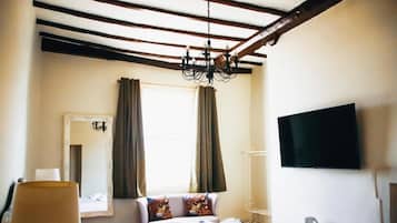 Quarto de hotel com cama, televisão, mesa de cabeceira, abajur e janela com cortinas.