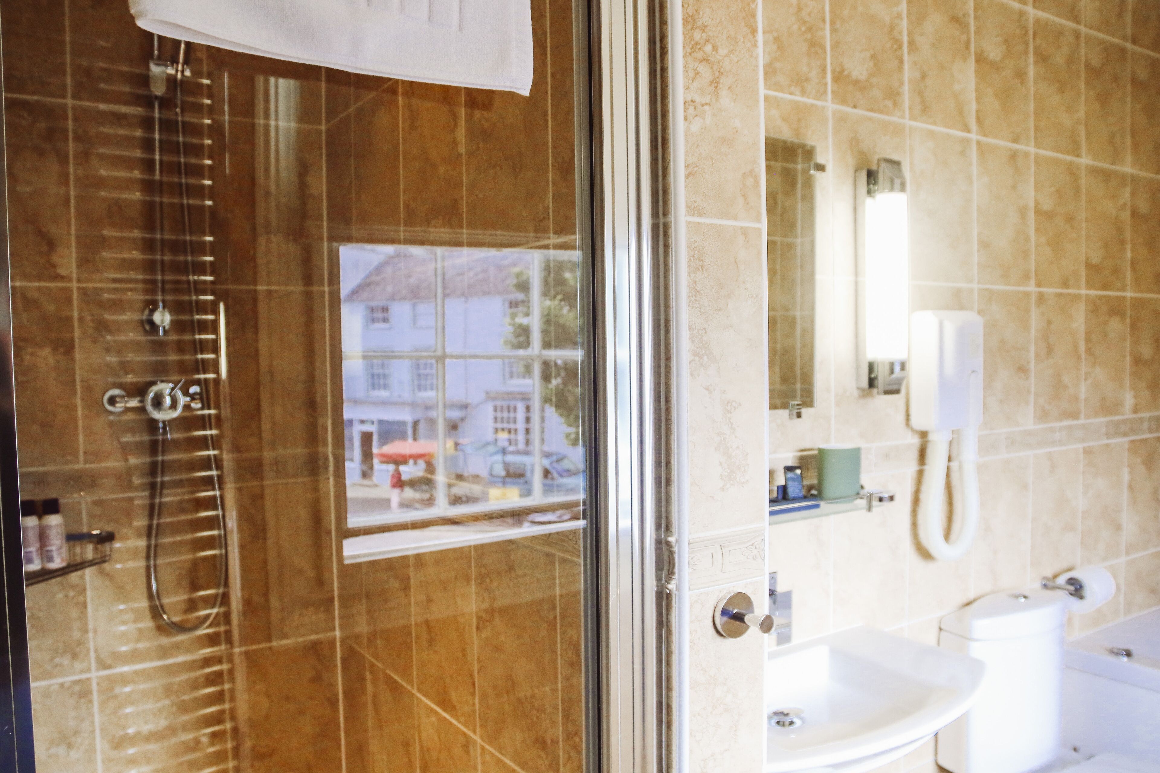 A bathroom with a shower, sink, toilet, and a window with a view of buildings outside.