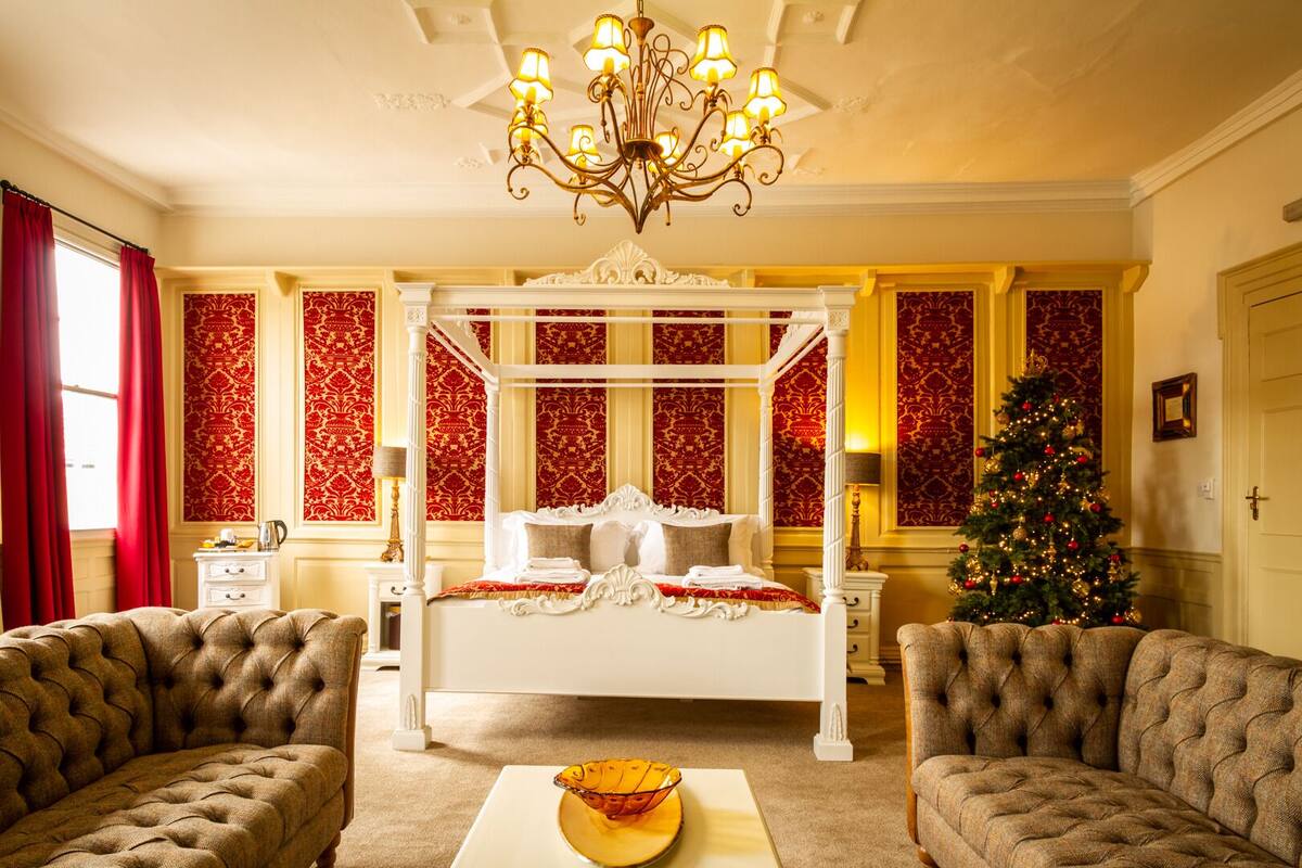 A luxurious bedroom with a four-poster bed, a chandelier, and a Christmas tree.