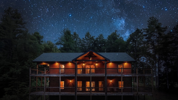 Uma cabana de toras de dois andares, com várias varandas e um céu estrelado acima.