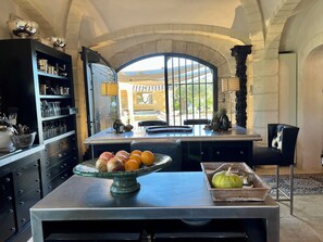 Une cuisine dotée d’un îlot central, d’un meuble noir contenant de la verrerie, et offrant une vue à travers une grande fenêtre en arc de cercle.