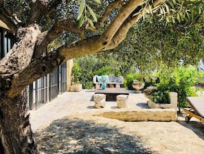 A patio area with a stone bench, a table, and a large tree providing shade.