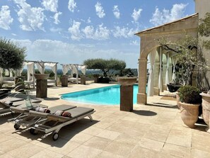 A pool area with lounge chairs, a pergola, and a view of the landscape.