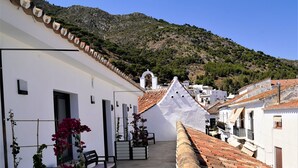 A narrow alleyway with terracotta tiled roofs, white buildings, and a mountainous backdrop.