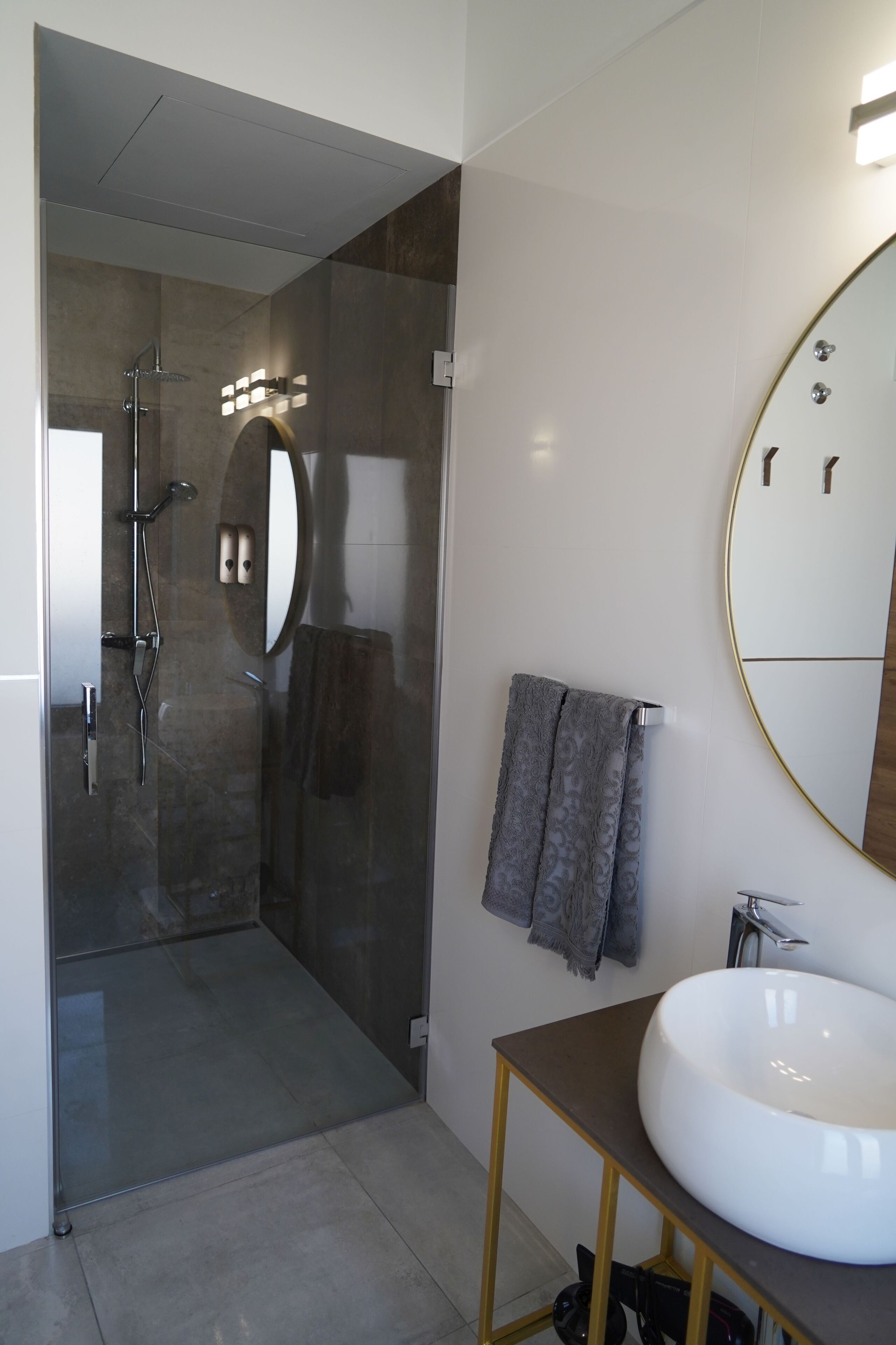 Un baño moderno con ducha acristalada, un espejo grande y un lavabo blanco sobre un mueble de madera.