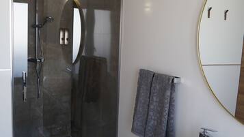 Un baño moderno con ducha acristalada, un espejo grande y un lavabo blanco sobre un mueble de madera.