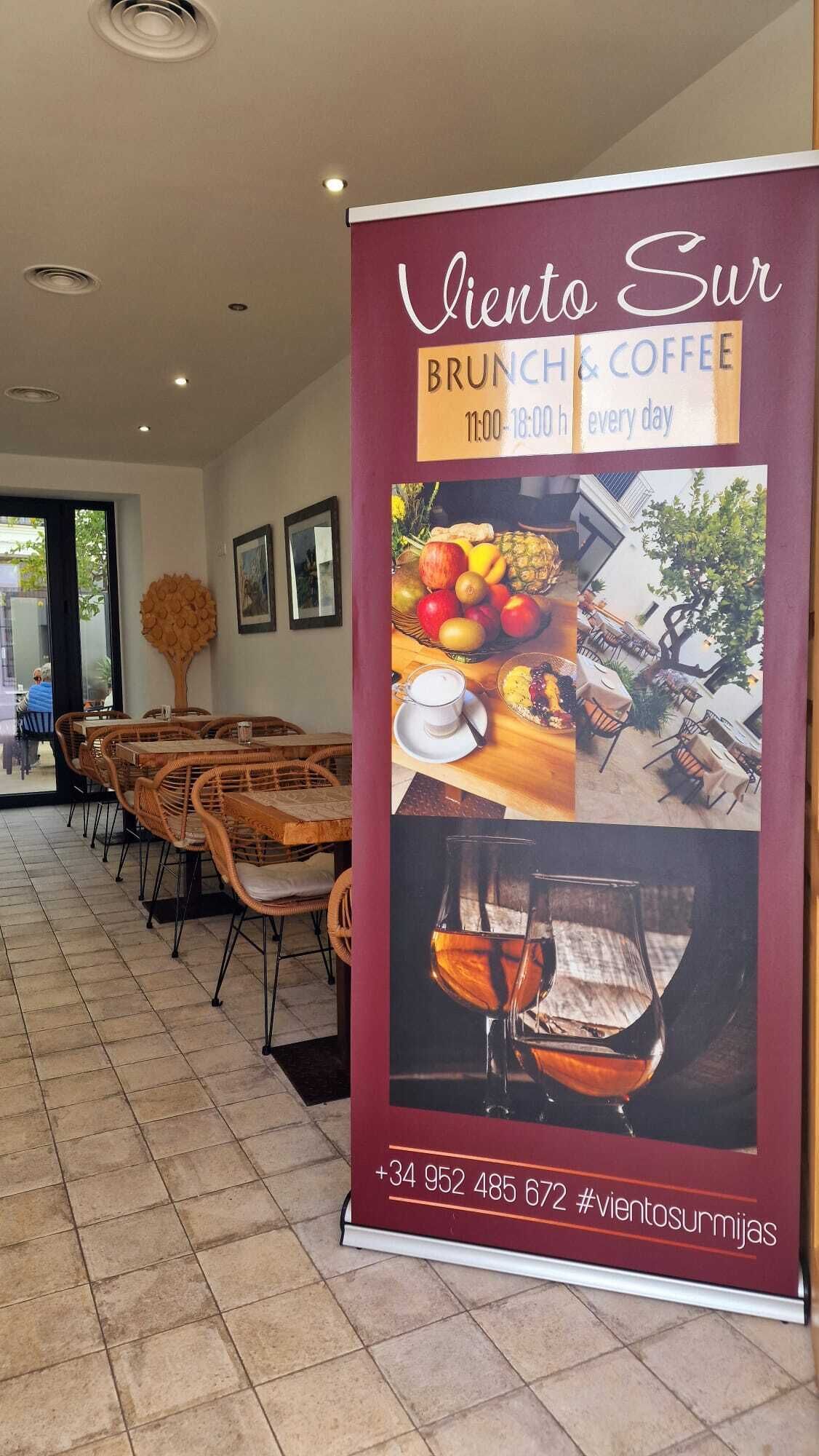 L’intérieur d’un restaurant, avec une enseigne indiquant « Viento Sur BRUNCH & COFFEE », ouvert tous les jours de 11h00 à 18h00.