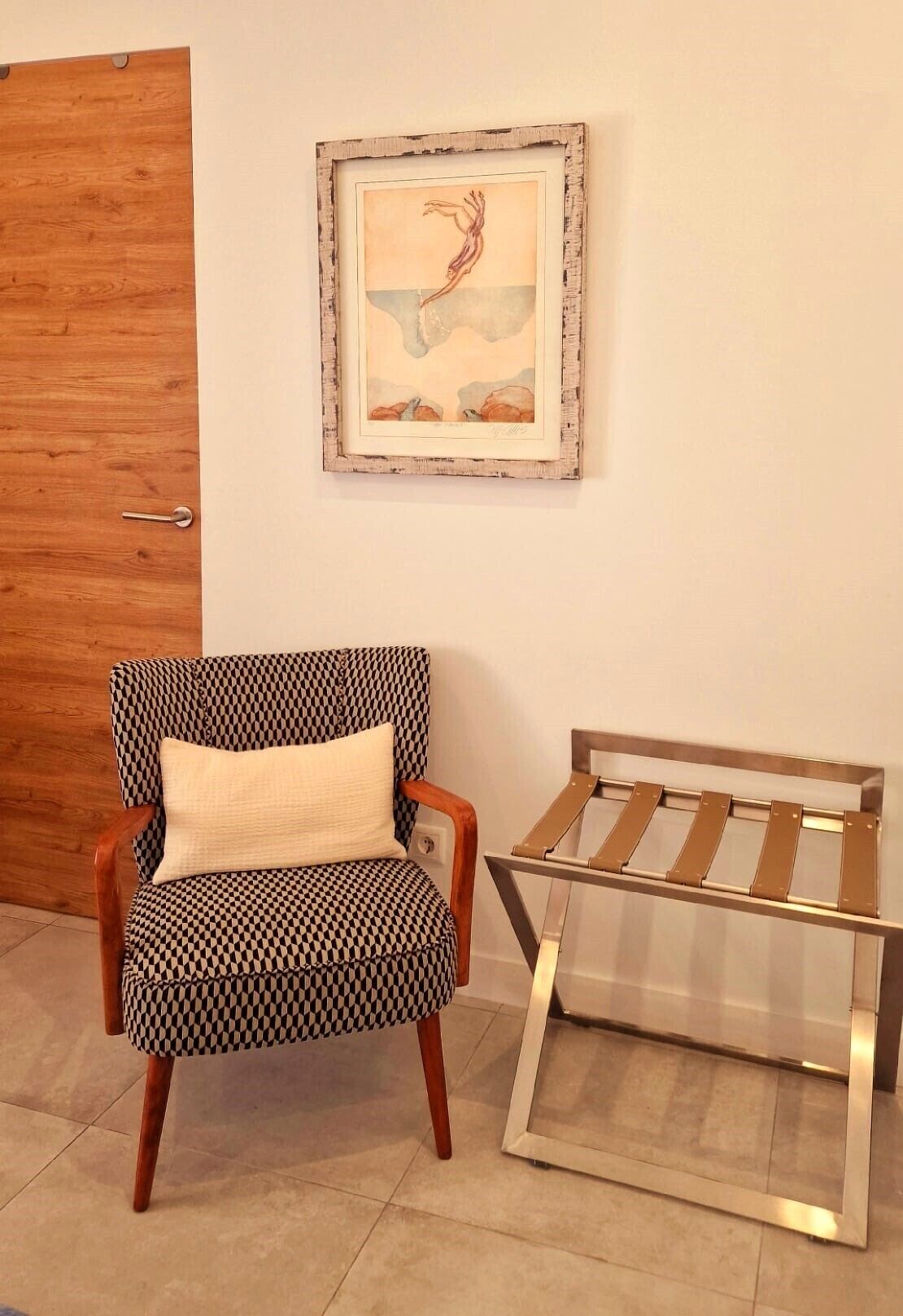 A room with a wooden door, a patterned armchair with a cushion, and a metal-framed table.