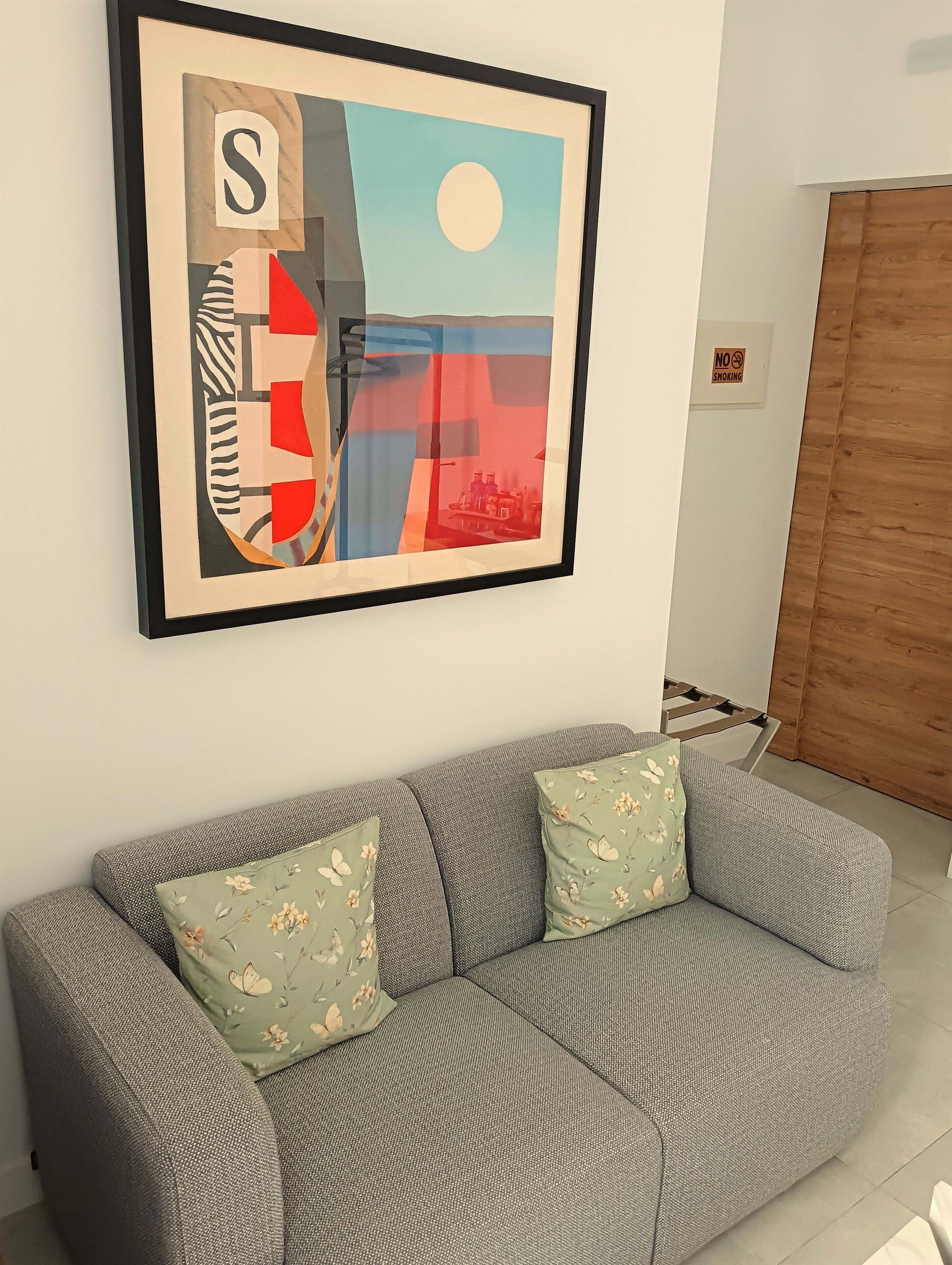 A framed abstract painting on a wall above a grey sofa with floral cushions.