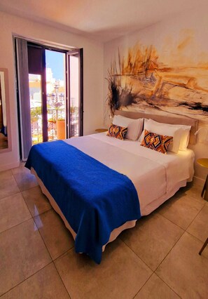 A hotel room with a large bed, a painting on the wall, and a balcony with a view of the city. - OPUNTIA Boutique hotel (Mijas)