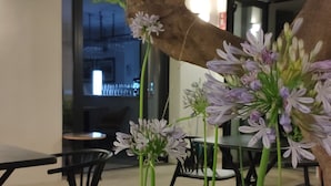 A modern indoor space with a dining area featuring black chairs and a table, surrounded by green plants and a tree with white flowers.
