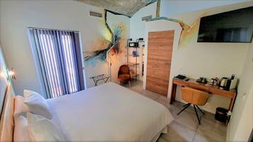 A hotel room with a large bed, a desk with a chair, a TV mounted on the wall, and a window with blinds.