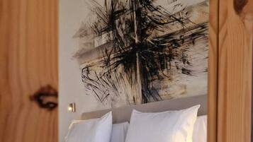 A bedroom with a bed, white bedding, and a large abstract painting on the wall.