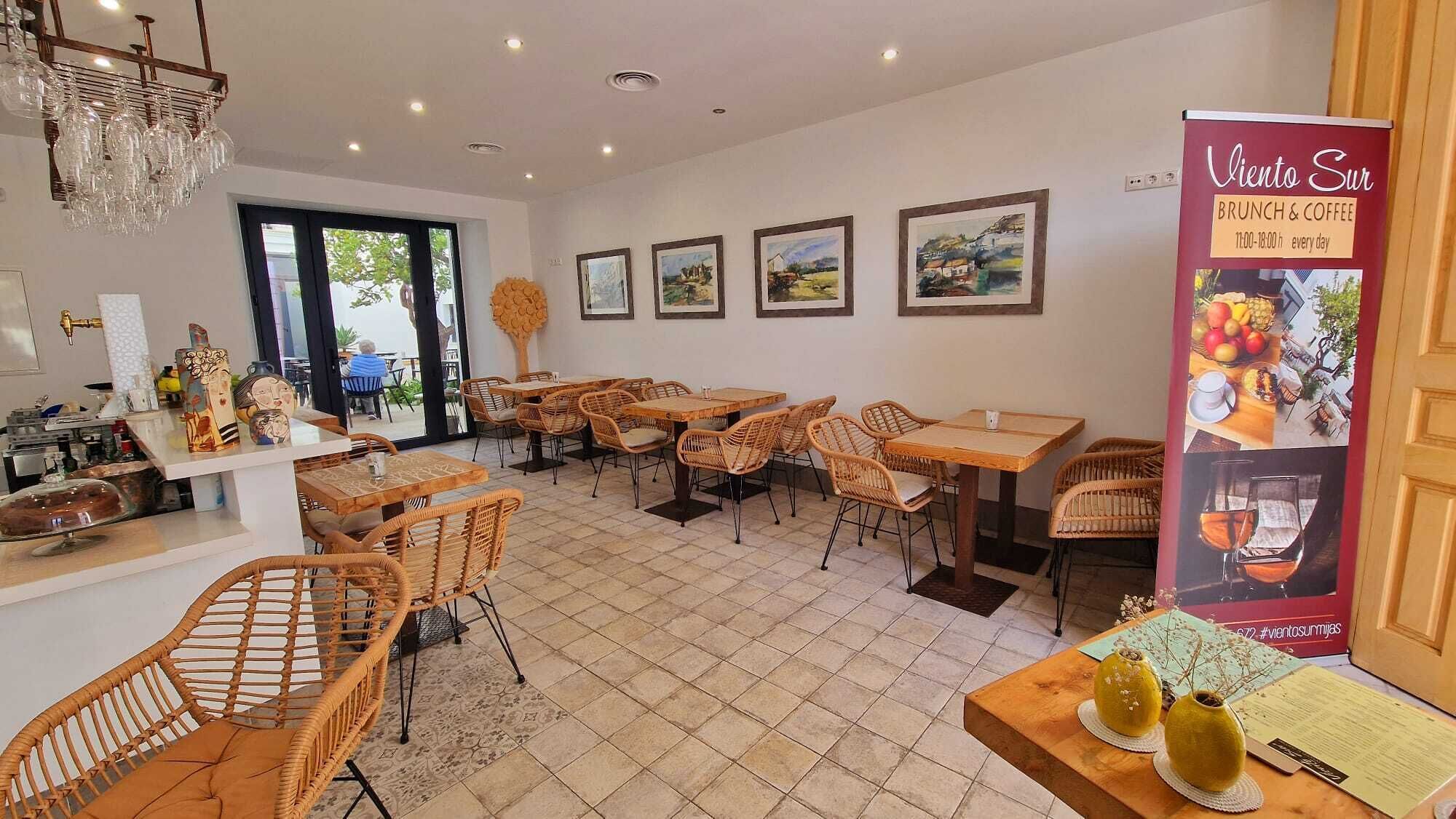 Restaurante com móveis de vime, lustre e quadros nas paredes.