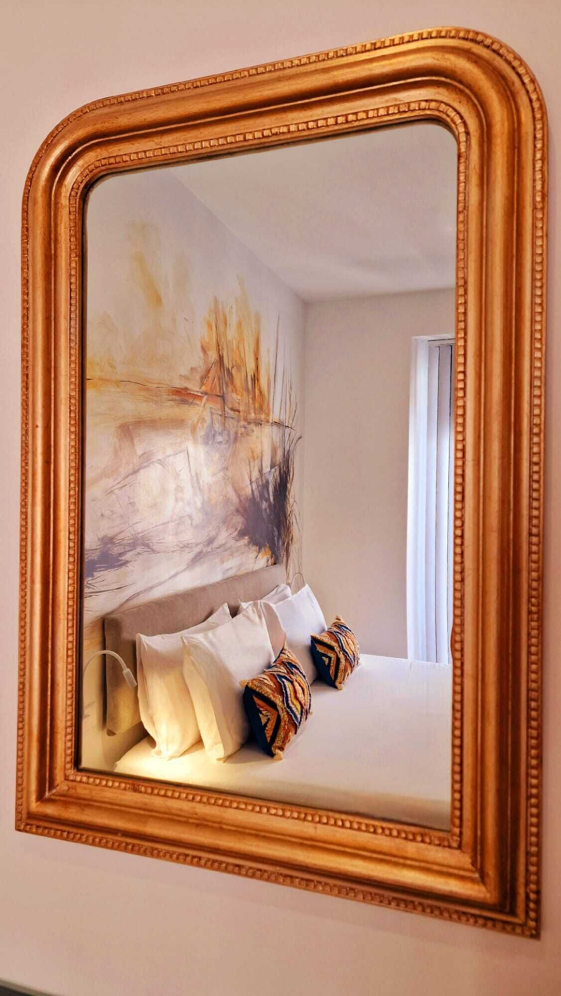 A bedroom with a large mirror, a bed with white linens, and a colorful abstract painting on the wall.