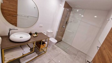 A modern bathroom with a white sink, a large mirror, a glass shower enclosure, and a wooden vanity.