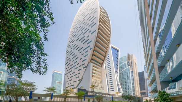 A modern building with a unique curved facade, a swimming pool, and surrounding greenery. - Tanin - Apartment Amidst Lively Area With Pool and Balcony (Dubai)
