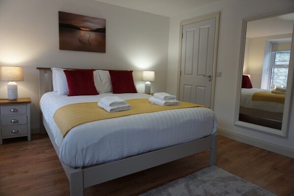 A neatly made bed with white and red pillows, a yellow blanket, and two folded towels on a wooden headboard. - ★ LUXURIOUS & NEW | in the heart of Donegal Town ★ (Donegal Town)