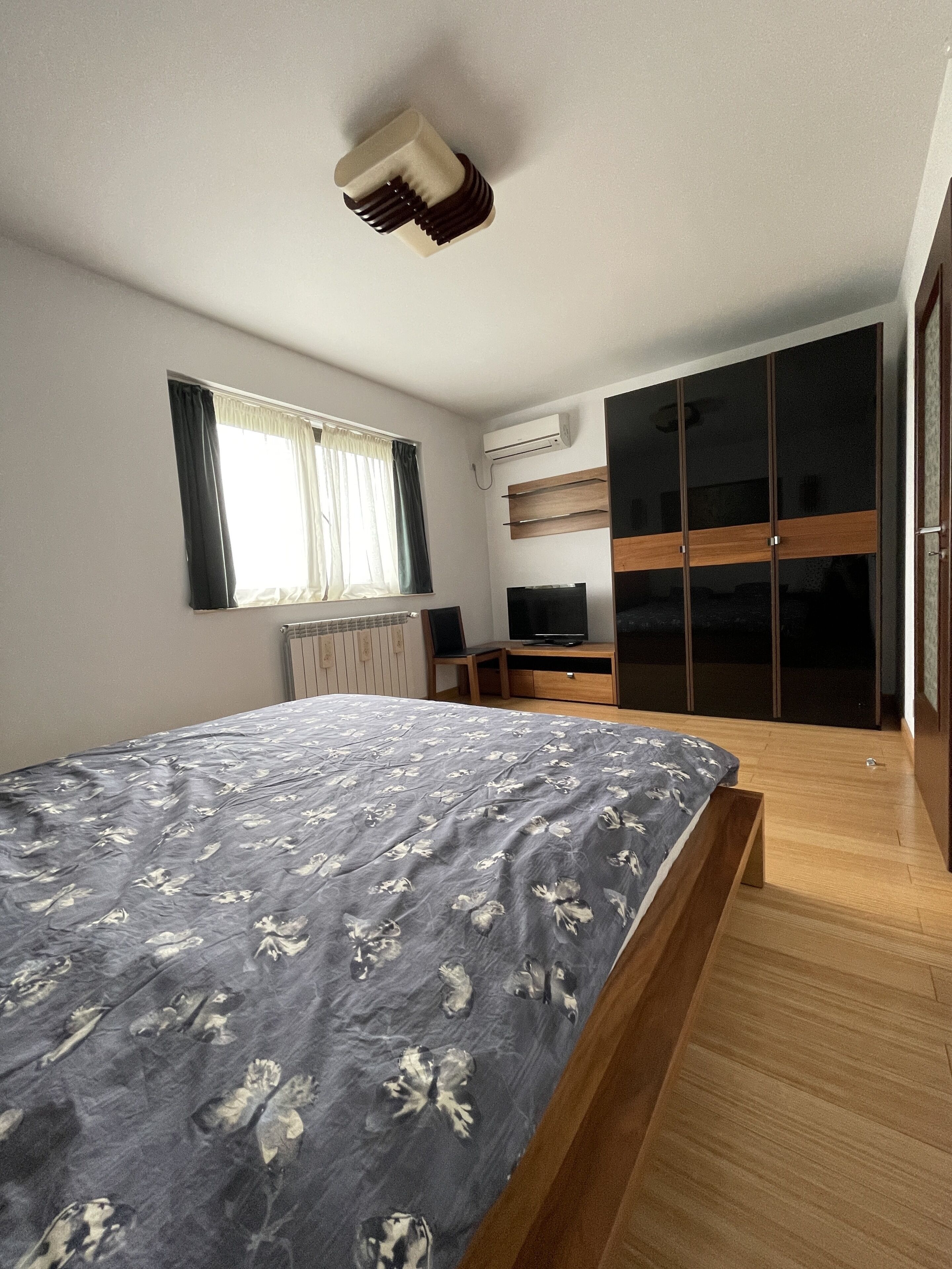 A bedroom with a bed, a TV, a wardrobe, and a window.