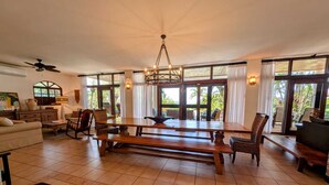 Un vaste espace de vie doté d’une grande table en bois, de sièges confortables et de larges fenêtres offrant une vue sur l’extérieur.