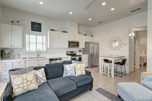 A modern kitchen with white cabinets, a stainless steel refrigerator, and a dining area with a small table and bar stools. - Pier 15: 2 Pools, Outdoor Dining, Covered Parking (Port Aransas)
