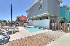A residential backyard with a swimming pool, wooden deck, and outdoor seating area. - Pier 15: 2 Pools, Outdoor Dining, Covered Parking (Port Aransas)