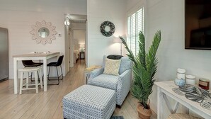A modern living room with a dining area, a large potted plant, and a wall-mounted TV. - Pier 15: 2 Pools, Outdoor Dining, Covered Parking (Port Aransas)