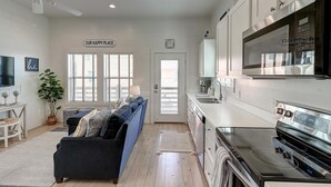 A modern kitchen with a Samsung refrigerator, a microwave, and a stainless steel stove. There is a blue sofa with cushions in the living area, a potted plant, and a sign that reads "OUR HAPPY PLACE". - Pier 15: 2 Pools, Outdoor Dining, Covered Parking (Port Aransas)