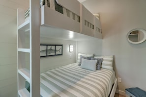 A bunk bed room with a striped bedspread, a framed shark picture, and a round mirror. - Pier 15: 2 Pools, Outdoor Dining, Covered Parking (Port Aransas)