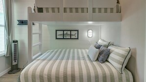 A bunk bed room with a striped bedspread, a framed shark picture, and a window with curtains. - Pier 15: 2 Pools, Outdoor Dining, Covered Parking (Port Aransas)