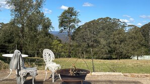 A rustic outdoor seating area with a metal fire pit, surrounded by a fence and trees.