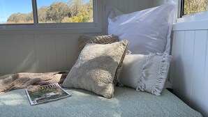 A cozy reading nook with a window view, a patterned throw blanket, and a magazine on the cushion.