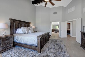 A bedroom with a wooden bed, two bedside tables, a ceiling fan, and a view into the bathroom.
