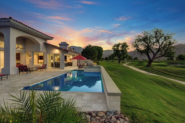 A modern house with a swimming pool, outdoor seating, and a view of the surrounding landscape.