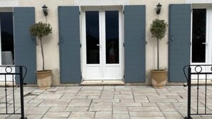 A building with a stone-paved entrance, a central door with glass panels, and two potted plants on either side. - Villa-mazet (Argilliers)