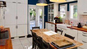 A modern kitchen with white cabinets, a wooden dining table, and pendant lighting. - Villa-mazet (Argilliers)