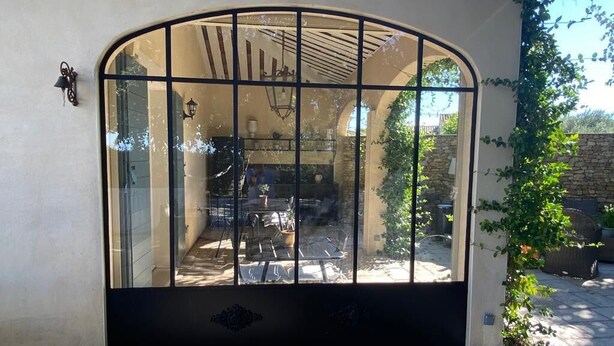 A patio area with a glass door leading to a kitchen, stone walls, and a hanging light fixture. - Villa-mazet (Argilliers)