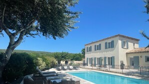 A poolside area with lounge chairs and a building with a tiled roof. - Villa-mazet (Argilliers)