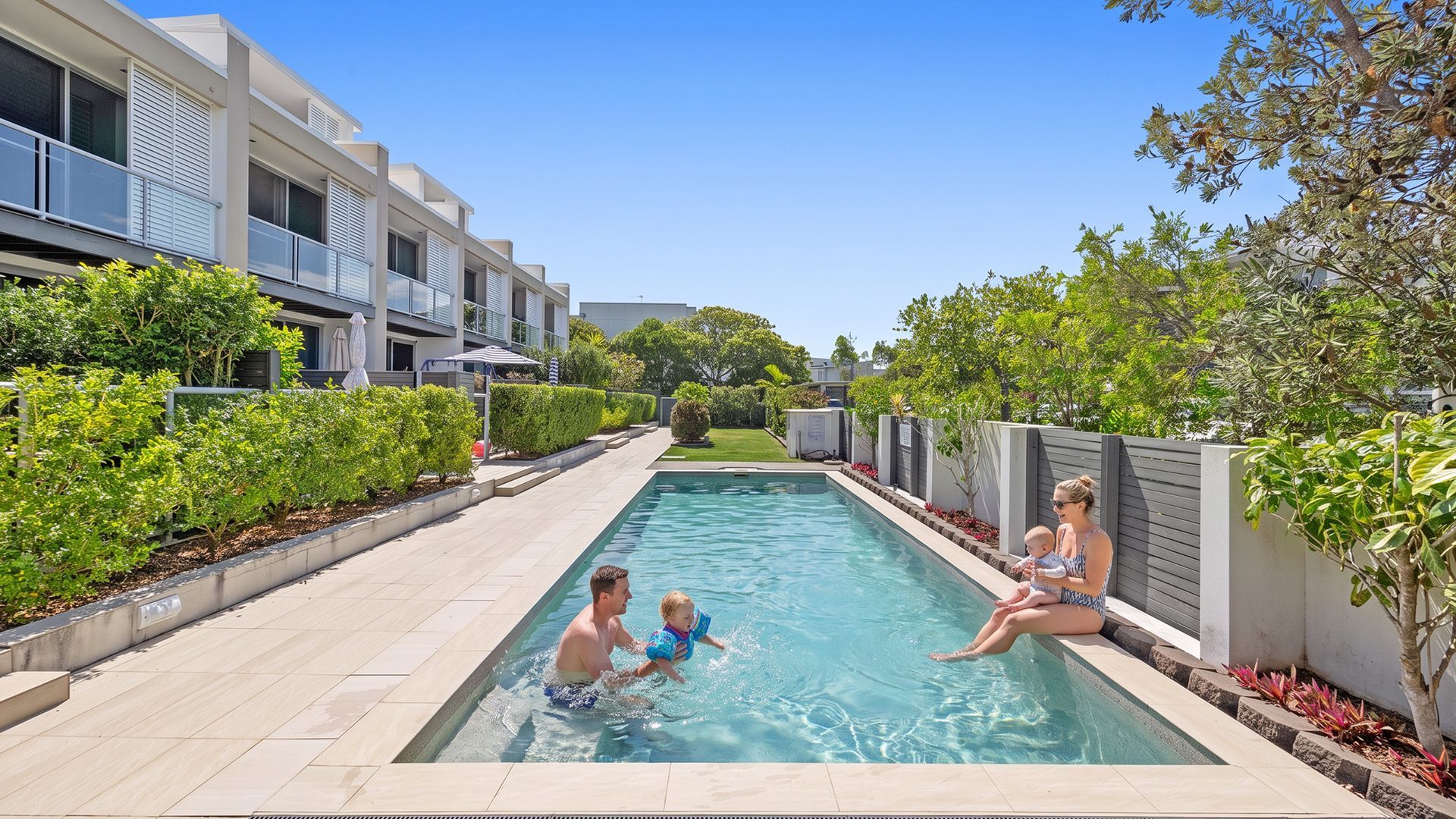 A swimming pool with a modern building in the background, surrounded by well-maintained greenery.