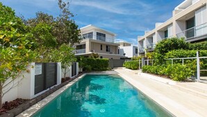 A modern residential building with a swimming pool, surrounded by greenery and a clear blue sky. - Beachside Haven Modern Townhouse with Pool (Casuarina)