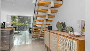 A modern kitchen with a wooden staircase, a glass door leading to a patio, and a decorative cabinet with a woven design. - Beachside Haven Modern Townhouse with Pool (Casuarina)