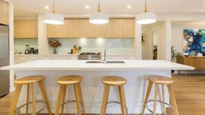 A modern kitchen with a large island, wooden stools, pendant lights, and a stainless steel sink. - Luxurious Privacy in Exquisite Home, Walk to Golf (Cowes)