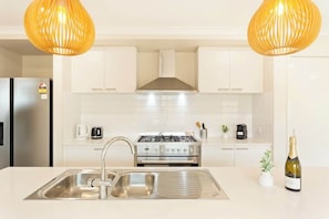 A modern kitchen with stainless steel appliances, a double sink, and pendant lighting.