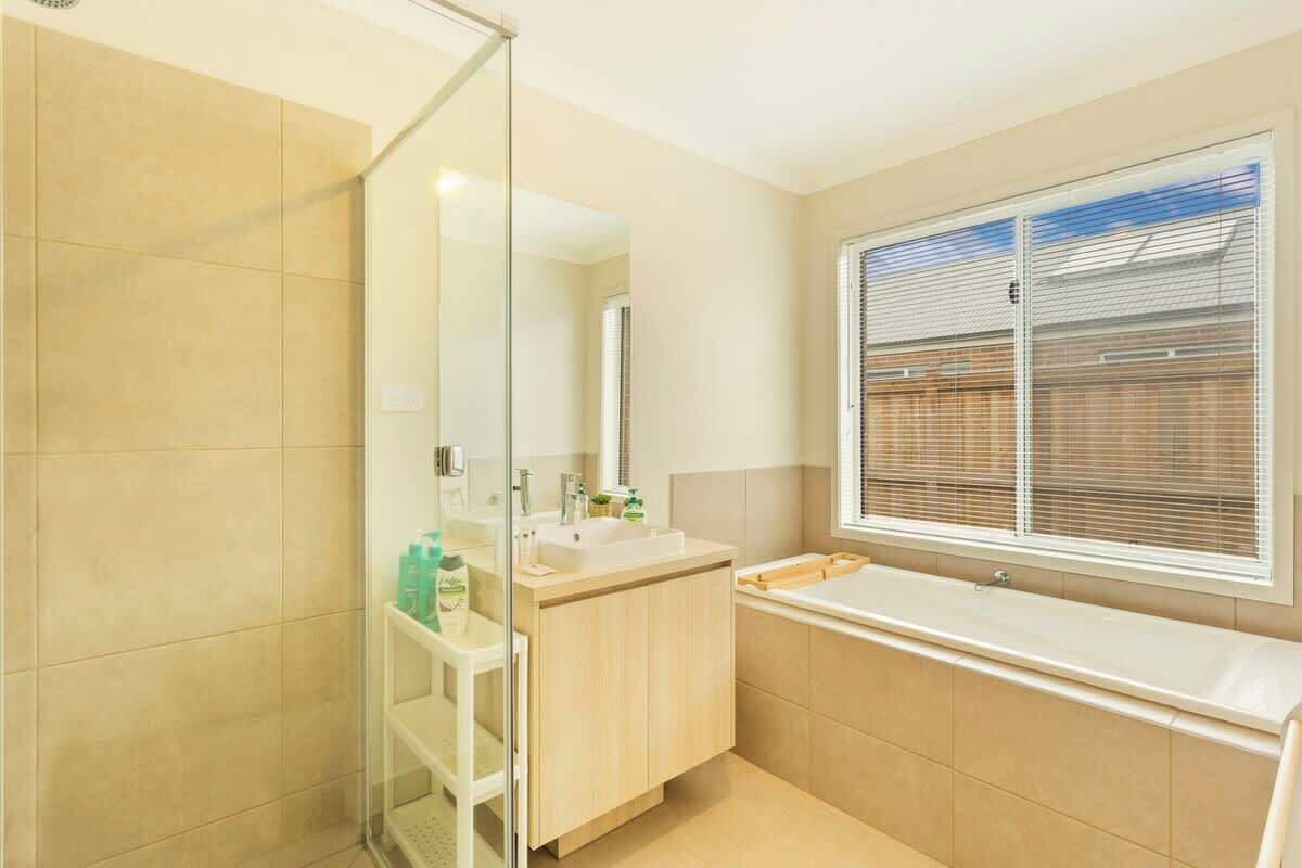 A modern bathroom with a glass shower enclosure, a sink with a mirror, and a window with blinds.