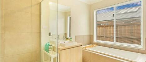 A modern bathroom with a glass shower enclosure, a sink with a mirror, and a window with blinds.