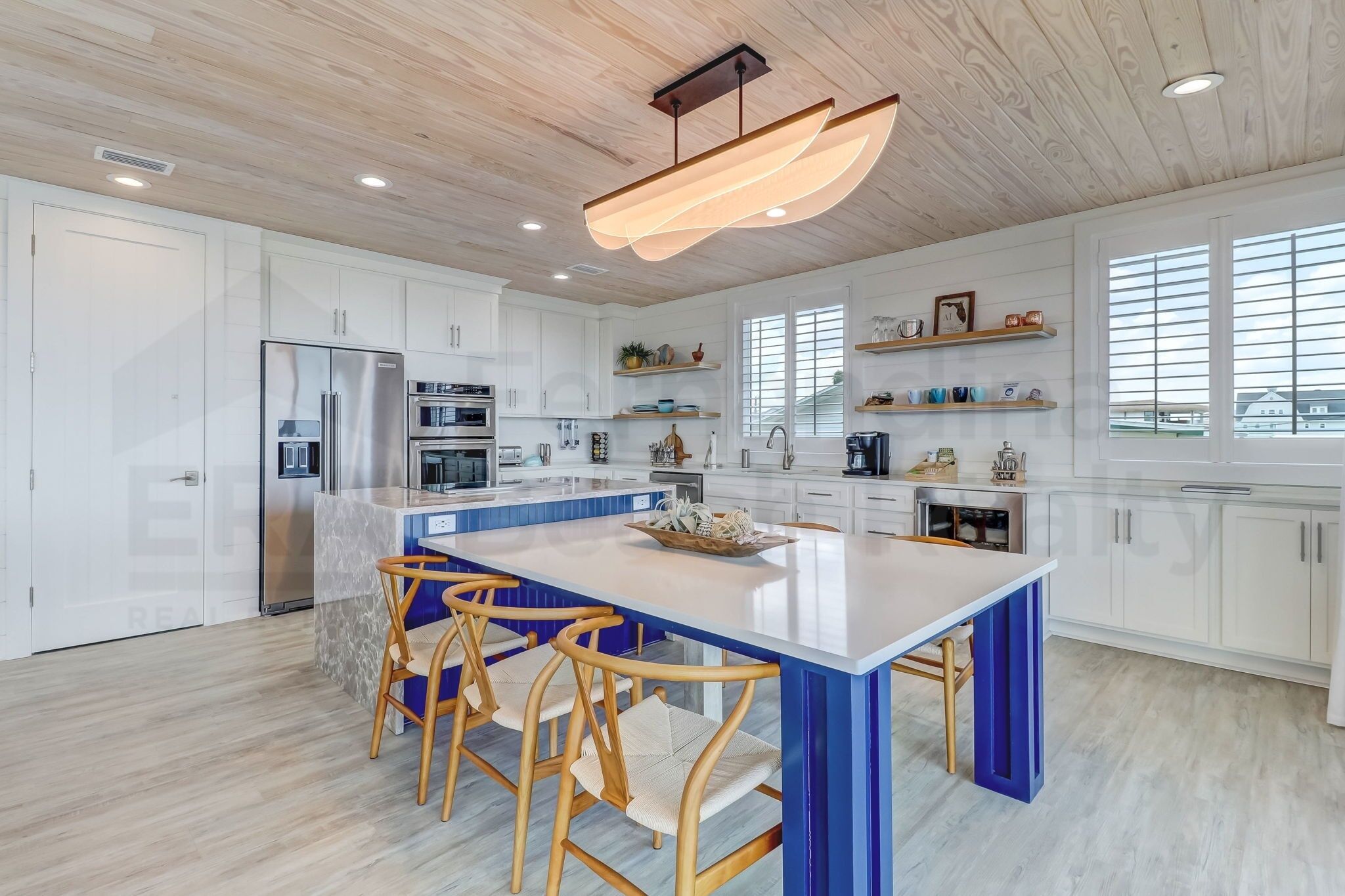Una cocina moderna con armarios blancos, una isla central con taburetes altos y una lámpara colgante.