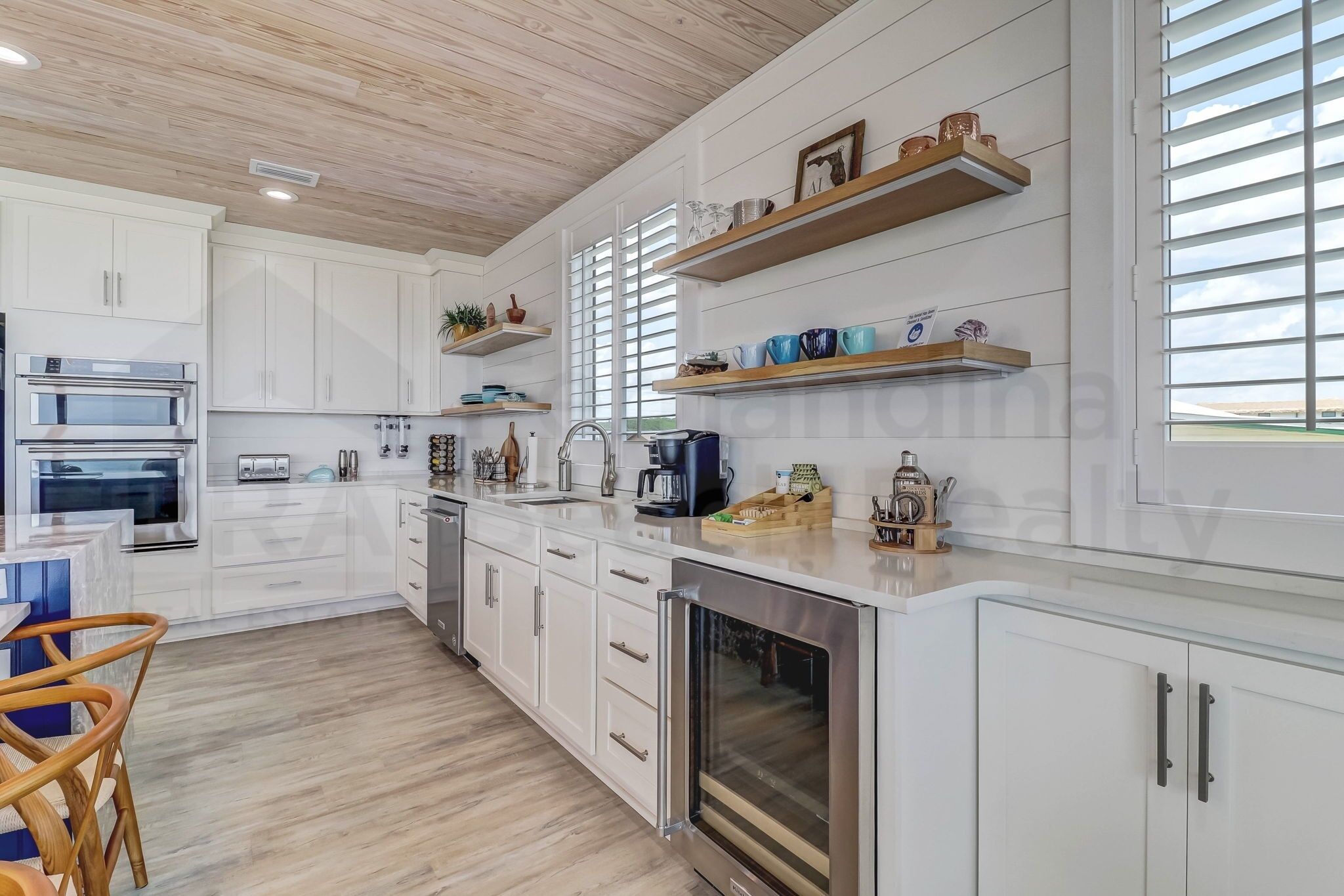 A modern kitchen with white cabinetry, stainless steel appliances, and wooden shelves.